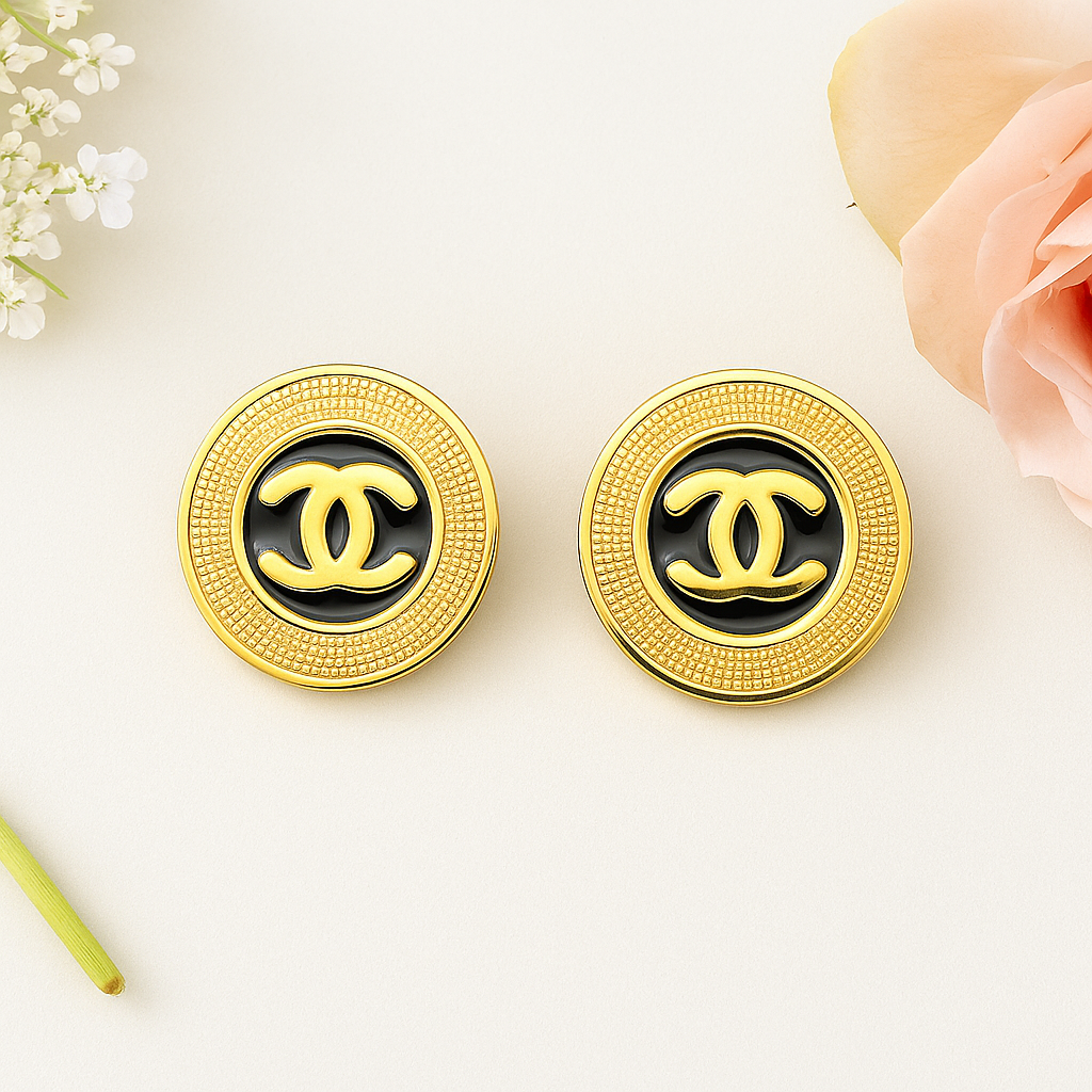 Gold and black Chanel earrings on a light background with flowers.