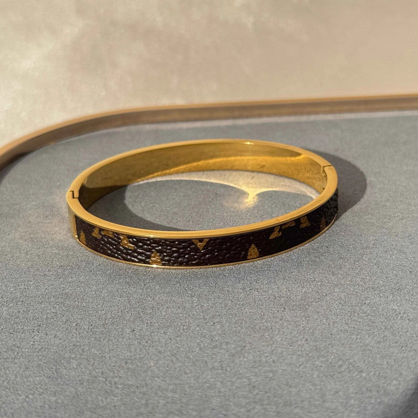 A 18K gold plated LV bangle bracelet with black patterned detailing presented on a display stand.