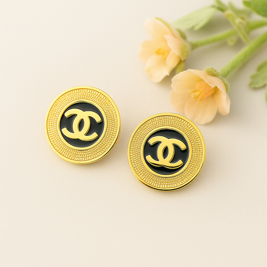 Gold and black Chanel earrings on a light background with flowers.