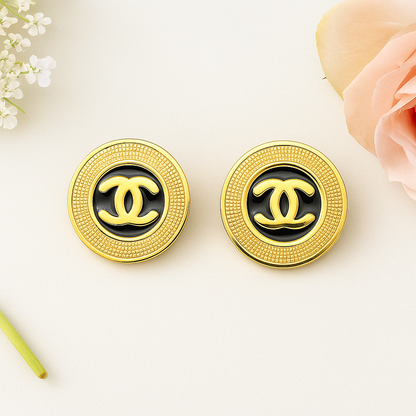 Gold and black Chanel earrings on a light background with flowers.