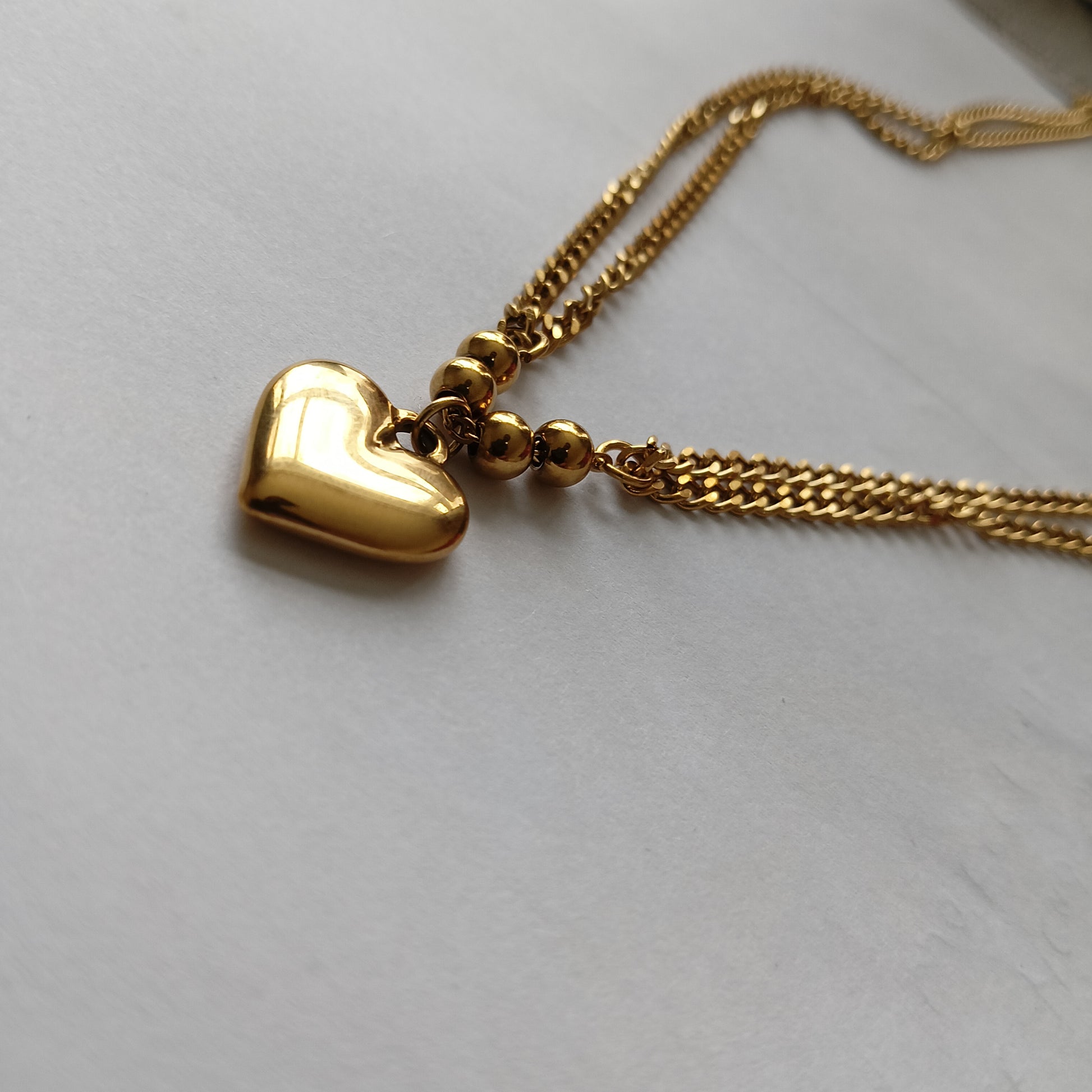 Gold heart-shaped pendant on a chain against a light gray background